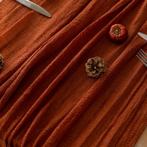 Rustic table setting with textured cloth, pinecones, and small pumpkins.