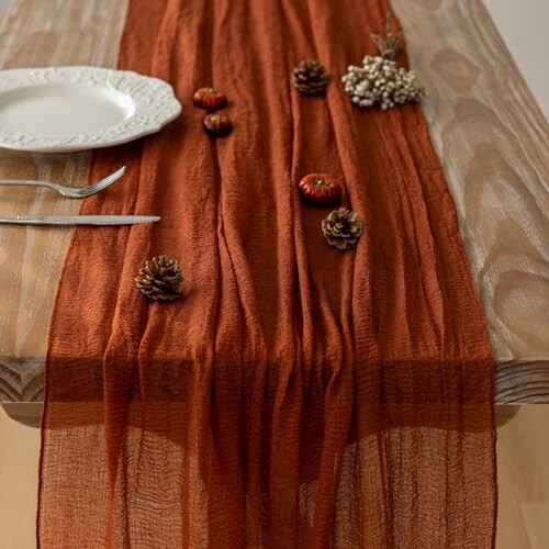 Rustic autumn table setting with orange table runner, pinecones, and small pumpkins.